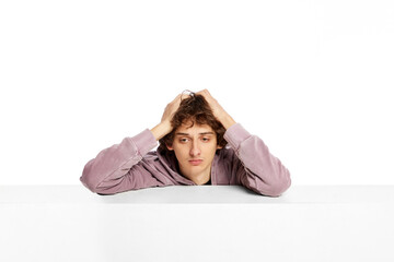 Portrait of young sad boy holding head with hands over white background. Suffering from sadness,...