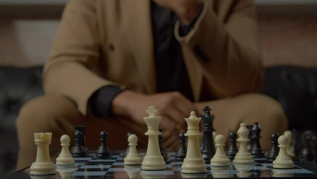 Close-up of black male businessman hand moving black chess queen piece on chessboard and checkmate opponent during chess competition.