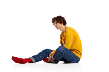 Portrait of young boy sitting on floor in sadness, feeling asocial over white background. Loneliness, depression