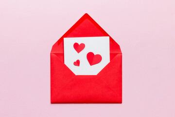 Red paper envelope with empty white card and heart on colored background. top view valentines day concept