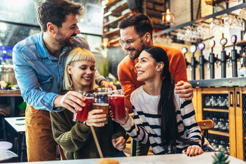 Smiling young friends drinking craft beer in pub
