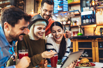 Young friends looking at digital tablet while sitting in cafe.