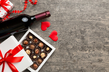 Bottle of red wine on colored background for Valentine Day with gift and chocolate. Heart shaped with gift box of chocolates top view with copy space