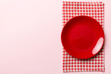 Top view on colored background empty round red plate on tablecloth for food. Empty dish on napkin with space for your design