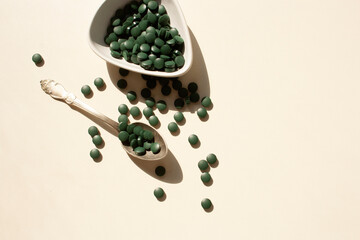Spirulina tablets in a spoon on a white background with contrast shadows. Flat style.
