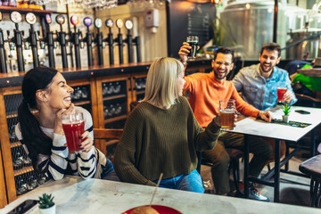 Smiling young friends drinking craft beer in pub