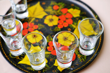 Empty glasses for alcohol stand on a tray painted in the old Russian style. Shots are ready to meet guests