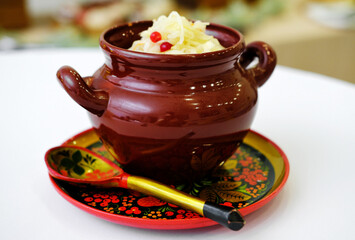 Sauerkraut in a clay pot on a wooden plate with a spoon in Russian old style