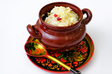 Sauerkraut in a clay pot on a wooden plate with a spoon in Russian old style.