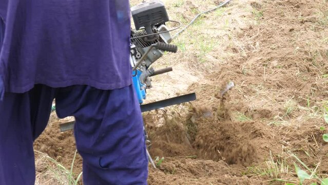 View Behind Pakistani Farmer Pushing Petrol Tiller Cultivator Over Ground Soil In Sindh, Pakistan. Slow Motion