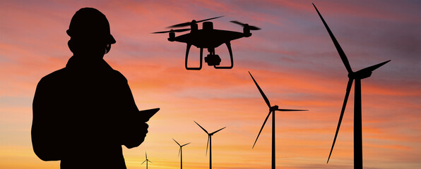 Silhouette of engineer with tablet computer, drone and wind turbines at sunset