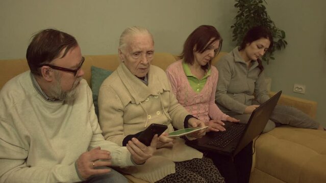 Family members use smartphones, tablet pc ( green screen ) and laptop. Slow motion 2x. An elderly man, a grandmother, a middle-aged woman and a young woman are sitting on a sofa in a room.