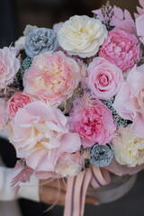 Beautiful spring flowers in box on woman hands. Preserved arrangement in grey round box. Women's day.
