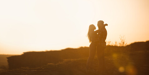 Silhouettes of man and woman in the mountains at sunset. Happy couple in love.	