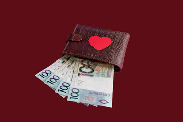 Brown leather wallet with red heart. Belarusian hundred-ruble bills stick out of the wallet. The concept of cash costs for the purchase of gifts for Valentine's Day, wedding, birthday. Close-up.