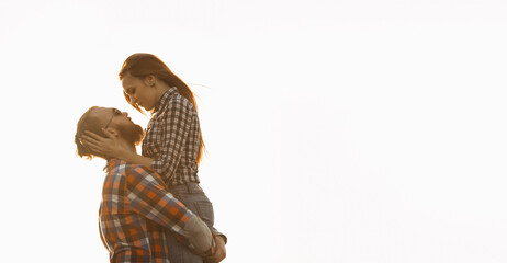 Bearded man and red-haired woman stand embracing at sunset.