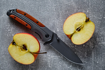 Folding knife for survival and two halves of cut apple.