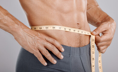 Man, body and tape measure on waist in studio on gray background. Health, fitness and male model with measuring tape for abdomen to track exercise training results, muscle goals or weight loss target