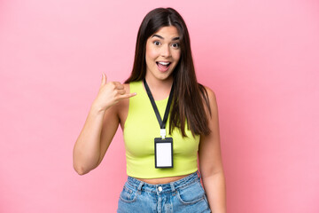 Young Brazilian woman with ID card isolated on pink background making phone gesture. Call me back...