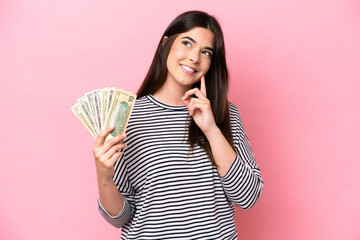 Young Brazilian woman taking a lot of money isolated on pink background thinking an idea while looking up