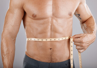 Man, body and tape measure on abdomen in studio on gray background. Health, fitness and male model...