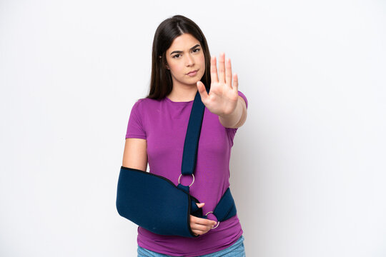 Young Brazilian woman with broken arm and wearing a sling isolated on white background making stop gesture