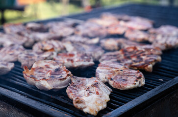closeup of pork slices being grilled on black iron barbeque grate outdoors