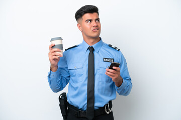 Naklejka premium Young police caucasian man isolated on white background holding coffee to take away and a mobile while thinking something