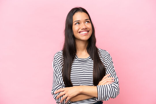 Young Colombian woman isolated on pink background looking up while smiling