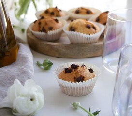 Muffins with chocolate sprinkles on a wooden stand near white ranunculus and a cup of tea