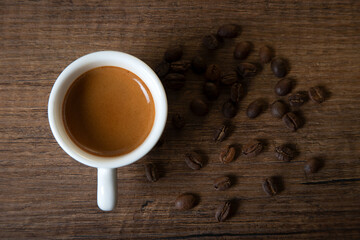 White cup of espresso with coffee beans on wooden table
