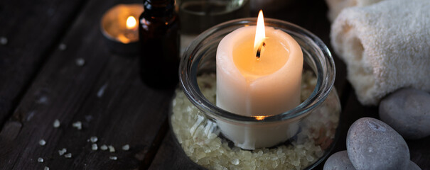 Spa setting with essential oil, candle, sea salt, pebbles, towel on dark wooden background. Massage, aromatherapy. Natural organic ingredients for relaxation, detention, wellness. Banner copy space