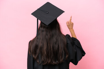Young university Colombian woman graduate isolated on pink background pointing back with the index...
