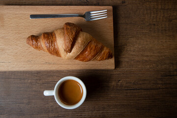 Croissant with espresso in white cup on wooden background