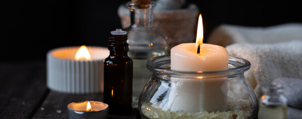 Spa setting with essential oil, candle, sea salt, pebbles, towel on dark wooden background. Massage, aromatherapy. Natural organic ingredients for relaxation, detention, wellness. Banner copy space
