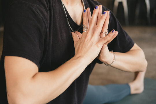 Side close-up photo of torso and hands of a female yogi new teacher in skandasana pose with hands to heart wearing green leggings in her yoga practice on a mat on the floor