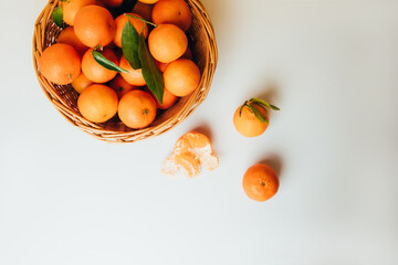 Orange mandarins clementine with green leaves in straw basket on a white-yellow background. Top view