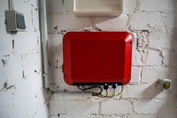 Red inverter of a photovoltaic system mounted on a white basement wall