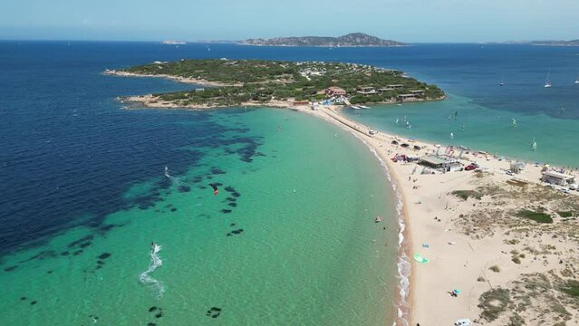 Windsurfer surfs along white sandy beach towards peninsula island at Porto Pollo, Sardinia - 4k Aerial