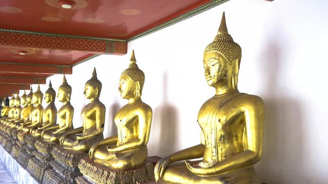 A row of golden Buddha sculptures in a temple in Thailand. Natural daylight, perspective view.