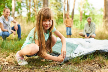 Girl setting up tent with family in nature