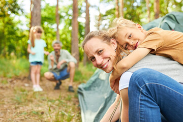 Happy son with mother setting up tent in forest