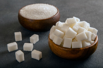 Cube sugar and granulated sugar on dark background,closeup