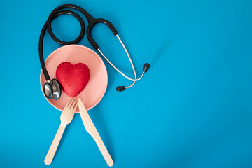 Flat lay composition with pink plate, stethoscope for heart-healthy diet on blue background
