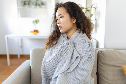 Sick young Asian woman feeling cold covered with blanket sit on bed, ill black girl shivering freezing warming at home wrapped with plaid, no central heating problem, fever temperature flu concept