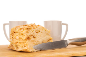One piece of cream cake on wooden tray with metal knife and two white cups, macro, isolated on white background.