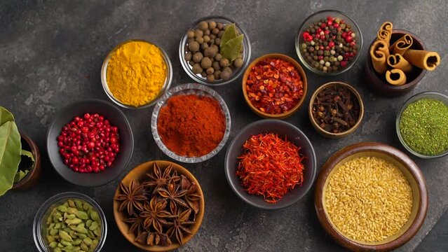 Set of Spices and herbs for cooking. Small bowls with colorful seasonings and spices - basil, pepper, saffron, salt, paprika, turmeric. On black stone table top view copy space
