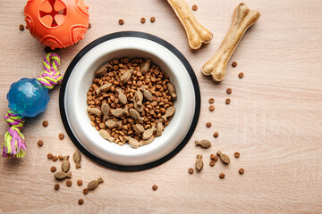 A bowl with dog food, dog treats and toys on a wooden floor.