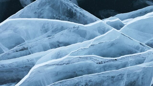 Beautiful natural pattern on the ice of frozen Baikal Lake in the form of white fault lines on the surface of transparent blue ice. movement rotation. Nature background. Close-up, flat lay, mock up
