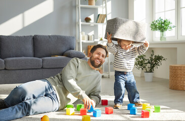 Happy, joyful bearded father together with his little child son playing with colorful toy blocks in...